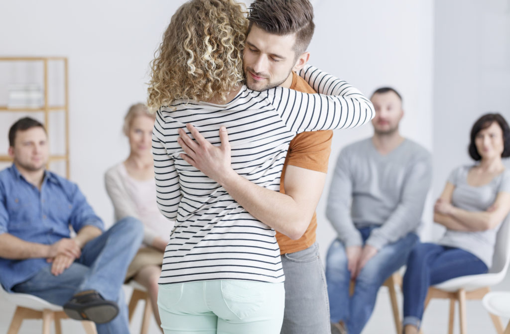 Young man hugs woman during support group community with other members in background