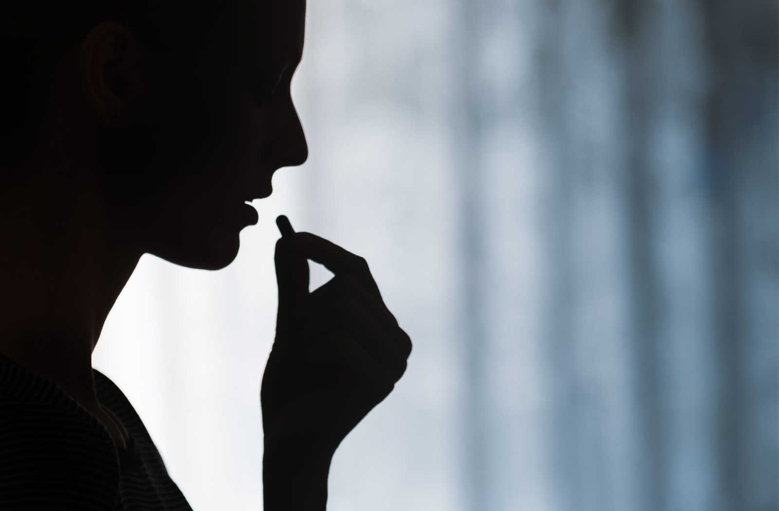 A dark, shadowy image of a person about to put a pill in their mouth.