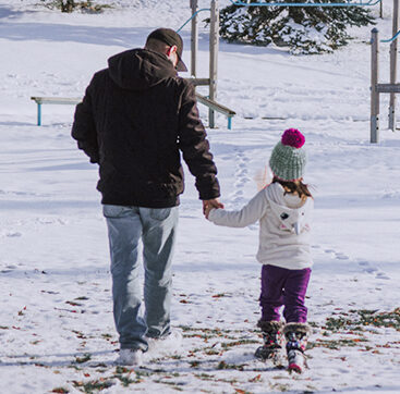 adult and child holding hands walking in the snowy park