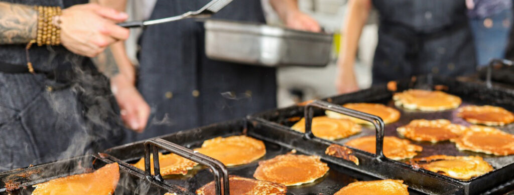 Golden pancakes on a grill being flipped by a person holding a spatula.